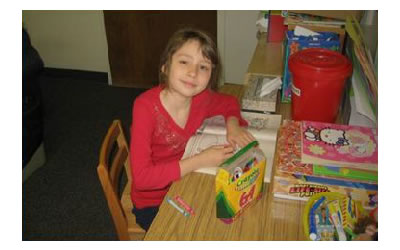 Katie seated at a desk with coloring books and crayons.