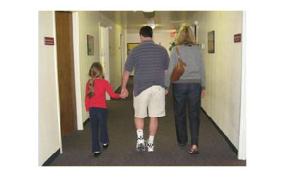 Katie and her parents in the hallway, walking away, holding hands.