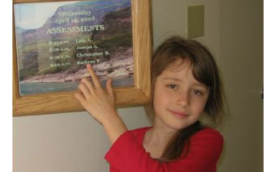 Katie pointing to the Assessments schedule posted on the wall.