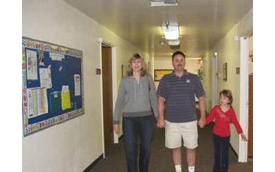 Katie and her parents walking in the indoor hallway, together, holding hands.
