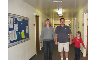 Katie and her parents walking in the indoor hallway, together, holding hands.
